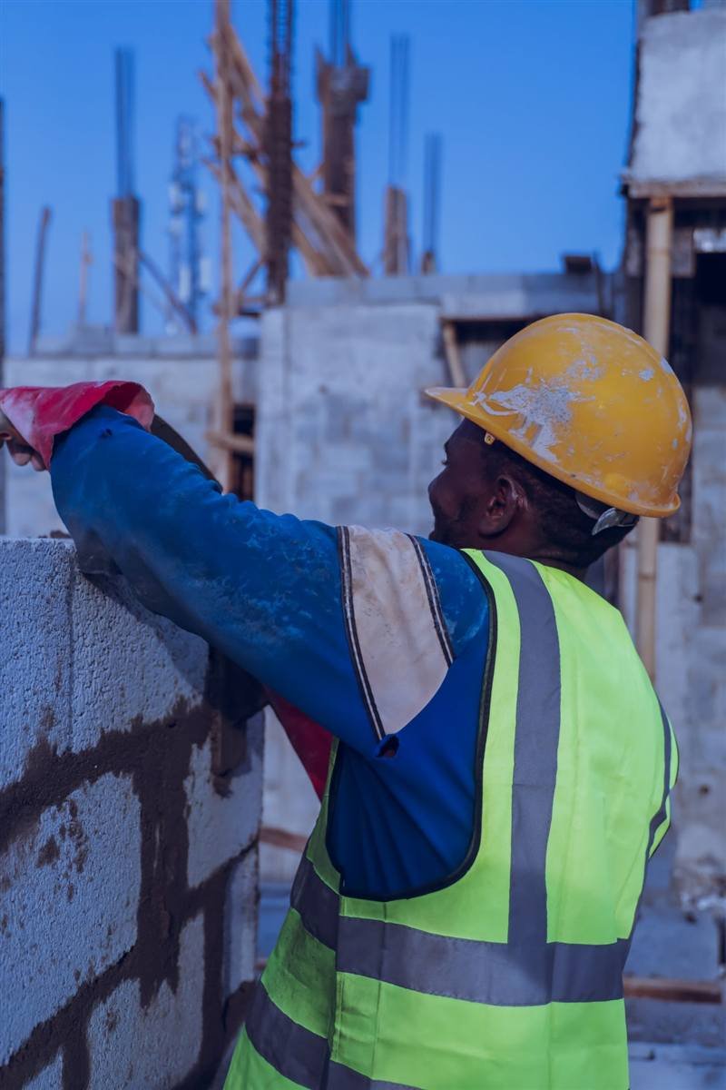 Mason in high-visibility vest building a block wall